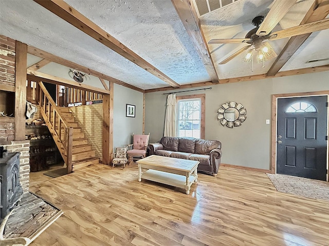 living room with visible vents, stairway, beamed ceiling, wood finished floors, and a wood stove