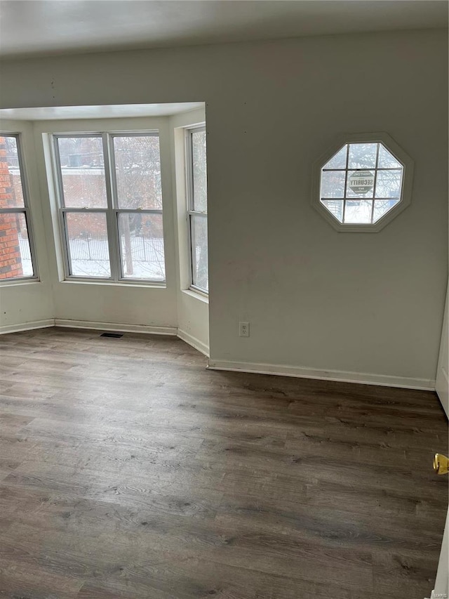 empty room featuring dark wood finished floors, visible vents, and a healthy amount of sunlight