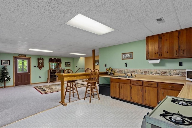kitchen with a paneled ceiling, light countertops, white microwave, brown cabinetry, and a sink