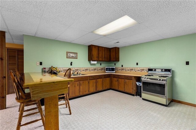 kitchen with white microwave, a paneled ceiling, a sink, light countertops, and gas range