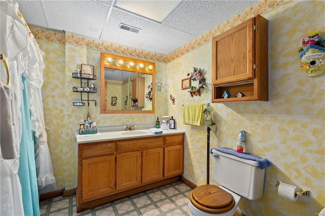 bathroom featuring a paneled ceiling, toilet, visible vents, vanity, and wallpapered walls