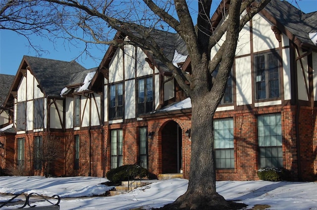 tudor home featuring stucco siding, roof with shingles, and brick siding