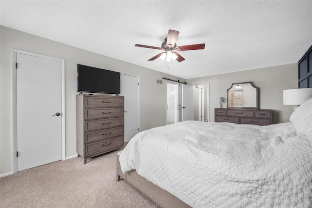 bedroom with visible vents, a barn door, a ceiling fan, light carpet, and a textured ceiling