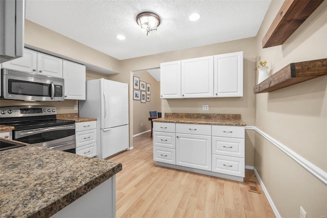 kitchen with light wood-type flooring, appliances with stainless steel finishes, dark countertops, and white cabinetry