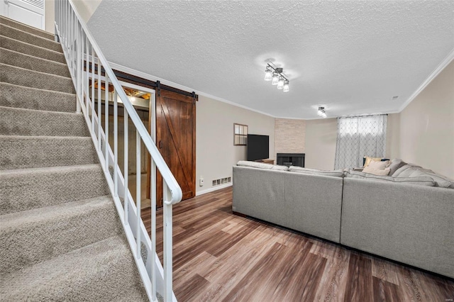 living room with a barn door, wood finished floors, visible vents, stairway, and crown molding