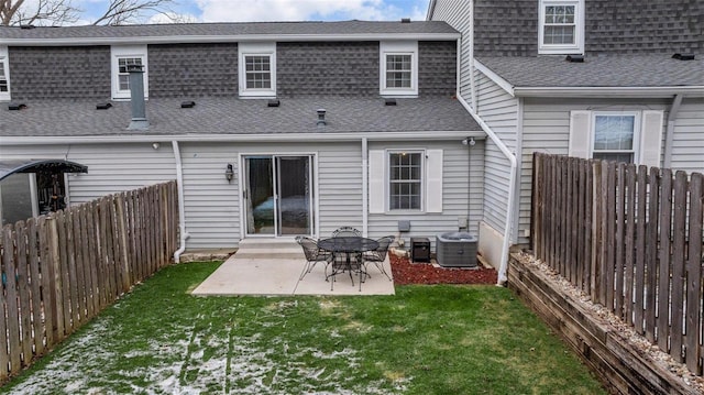 rear view of property with a lawn, a fenced backyard, roof with shingles, a patio area, and central AC