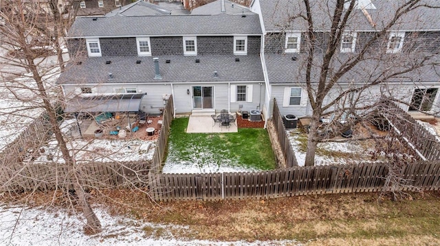 snow covered rear of property with central AC unit, a patio area, fence private yard, and a shingled roof