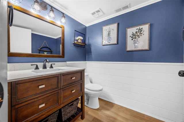 bathroom with toilet, wood finished floors, vanity, visible vents, and wainscoting