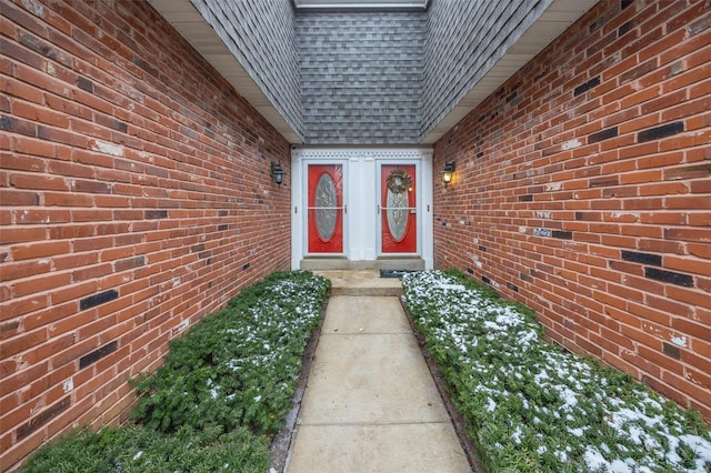 property entrance featuring brick siding, roof with shingles, and mansard roof