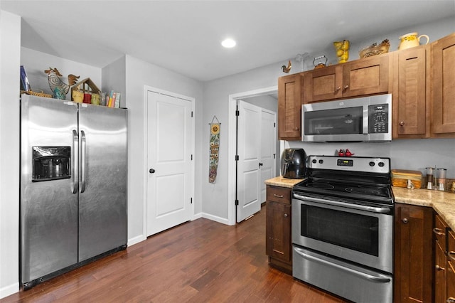 kitchen featuring baseboards, brown cabinetry, dark wood-type flooring, light stone countertops, and stainless steel appliances