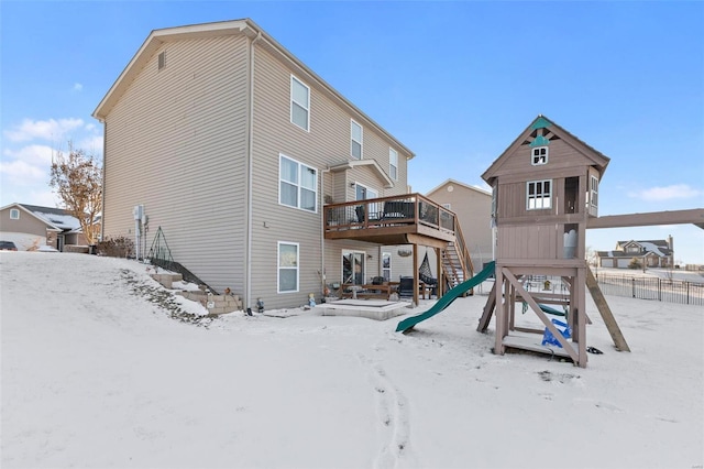 snow covered back of property featuring a playground and a wooden deck