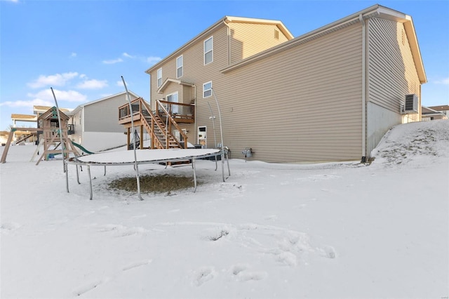 snow covered house featuring a deck, a playground, a garage, stairs, and a trampoline