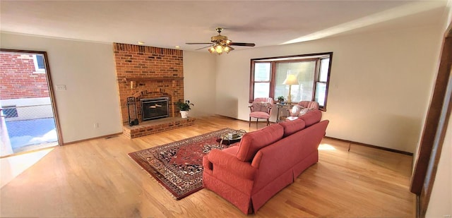 living area with light wood-style floors, ceiling fan, a brick fireplace, and baseboards