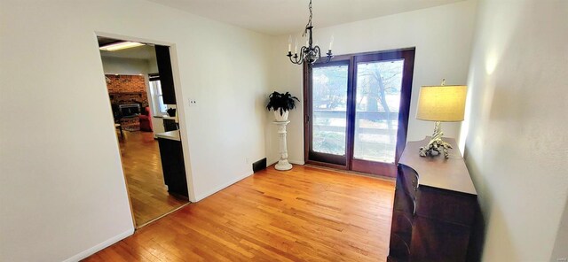 doorway featuring light wood-type flooring, baseboards, a chandelier, and a wealth of natural light