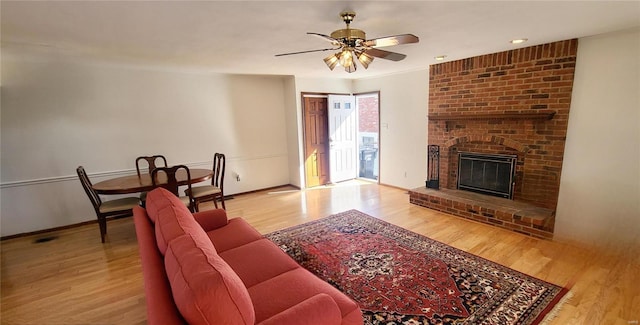 living area with a brick fireplace, wood finished floors, a ceiling fan, and baseboards