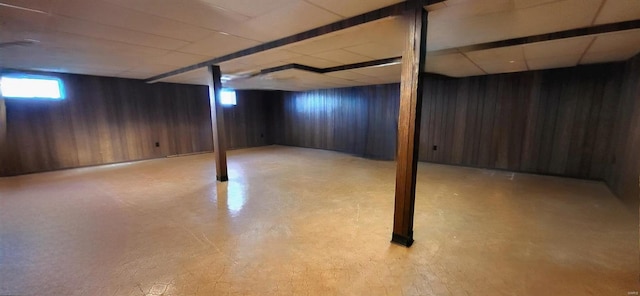 below grade area featuring a paneled ceiling, wood walls, and light floors