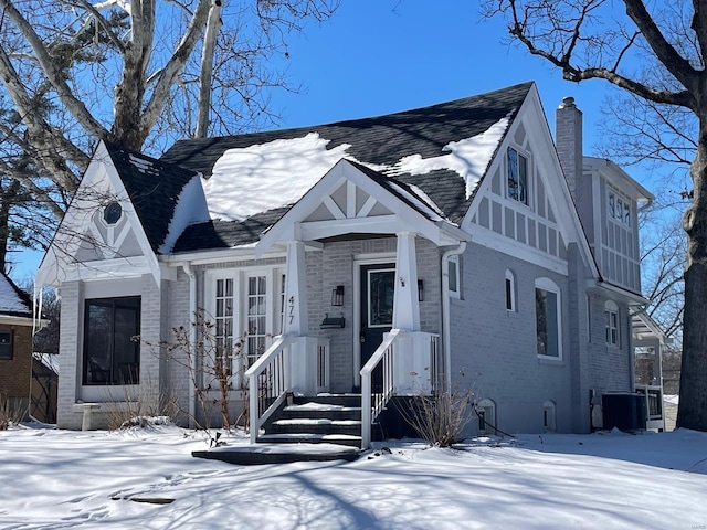 english style home with a chimney, cooling unit, and brick siding