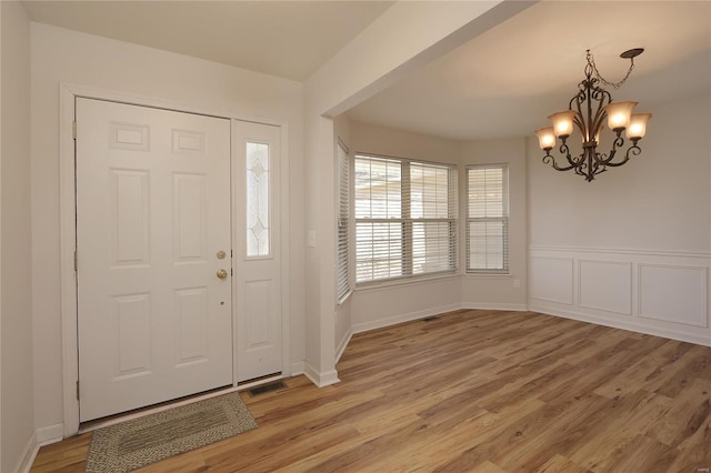 entrance foyer featuring visible vents, wainscoting, a chandelier, and light wood-style flooring