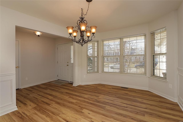 unfurnished dining area with light wood-style flooring, visible vents, baseboards, and a notable chandelier