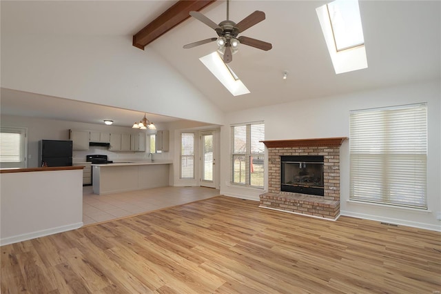 unfurnished living room with visible vents, beamed ceiling, light wood-type flooring, a brick fireplace, and ceiling fan with notable chandelier