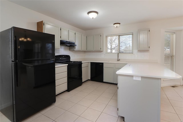 kitchen featuring light tile patterned floors, under cabinet range hood, a peninsula, a sink, and black appliances