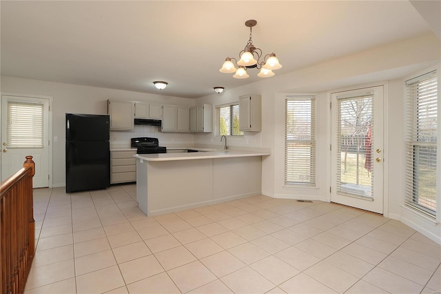 kitchen featuring a peninsula, under cabinet range hood, light countertops, black appliances, and a notable chandelier