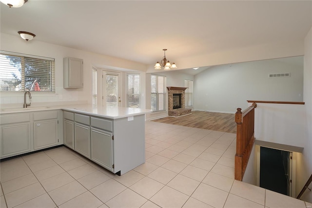 kitchen with light tile patterned floors, visible vents, a peninsula, light countertops, and a sink