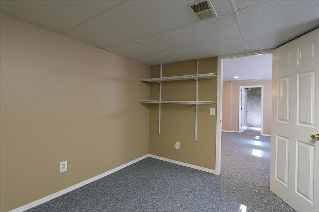 interior space featuring a paneled ceiling, dark carpet, visible vents, and baseboards