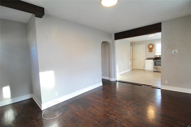 unfurnished room with arched walkways, wood-type flooring, beam ceiling, and baseboards