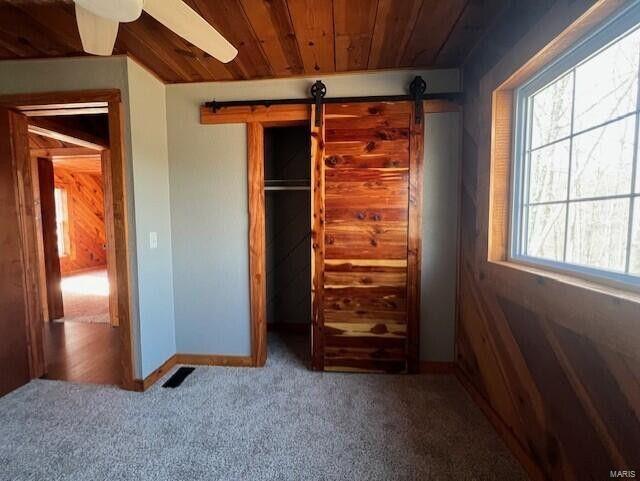 unfurnished bedroom featuring a barn door, wooden ceiling, carpet floors, visible vents, and baseboards