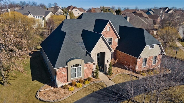 view of front facade with brick siding, roof with shingles, a chimney, a residential view, and stone siding