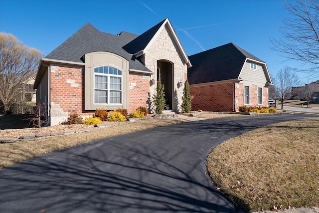 french provincial home featuring stone siding, brick siding, and a shingled roof