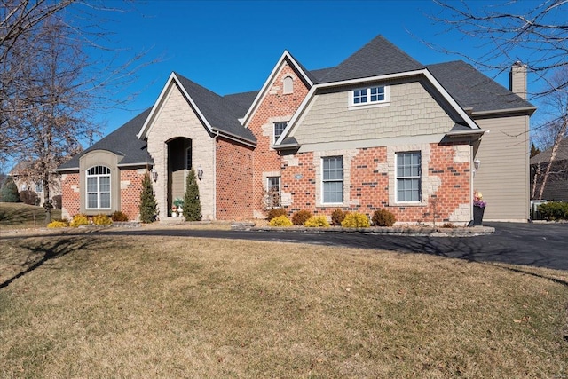 view of front facade with brick siding, a front lawn, a chimney, and a shingled roof