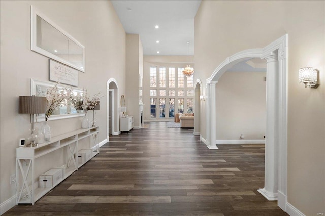 hallway with arched walkways, recessed lighting, a towering ceiling, wood finished floors, and baseboards