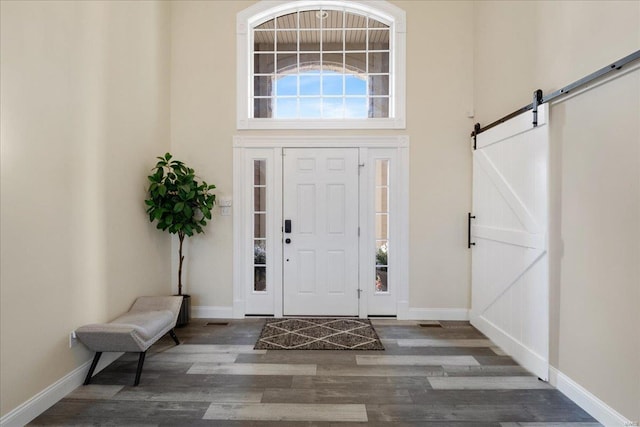 entryway featuring a barn door, baseboards, a high ceiling, and wood finished floors