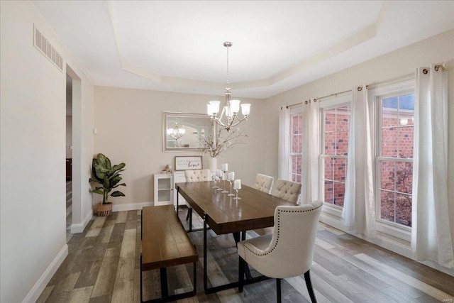 dining space with a tray ceiling, baseboards, an inviting chandelier, and wood finished floors