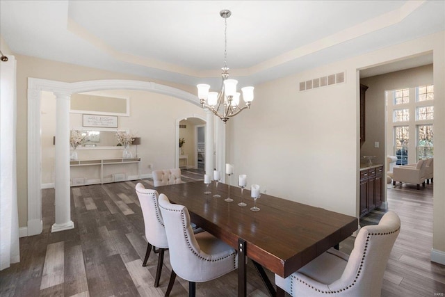 dining area featuring dark wood-style floors, a tray ceiling, visible vents, and arched walkways