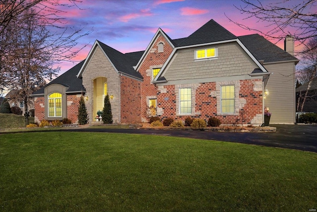 view of front of home featuring brick siding, a lawn, and a chimney