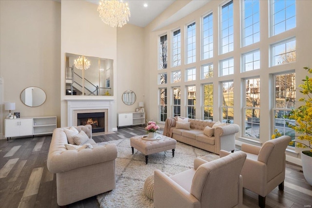 living room featuring a towering ceiling, dark wood-style floors, a fireplace with flush hearth, and a notable chandelier