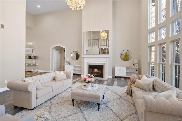 living room with arched walkways, a chandelier, a fireplace with flush hearth, wood finished floors, and baseboards