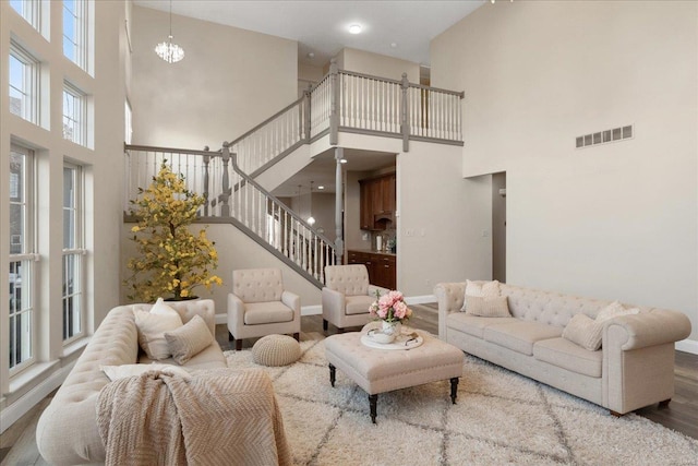 living room featuring a chandelier, wood finished floors, visible vents, baseboards, and stairway