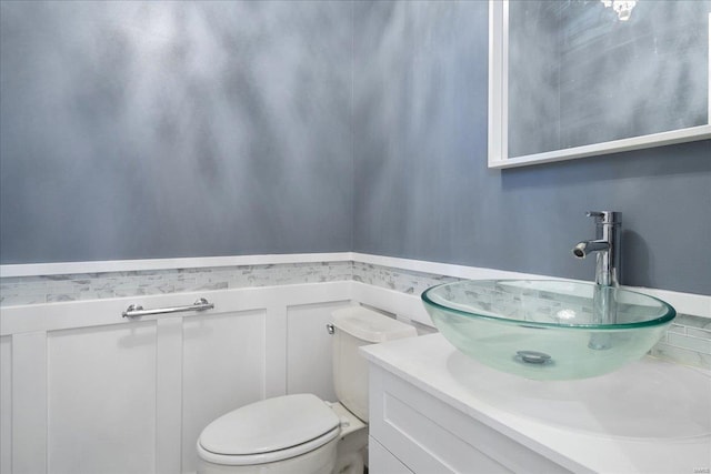 half bathroom featuring a wainscoted wall, vanity, and toilet