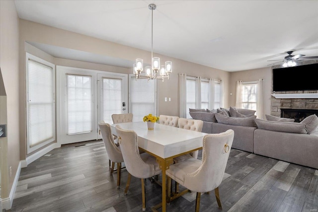 dining space featuring a fireplace, baseboards, dark wood-style flooring, and ceiling fan with notable chandelier