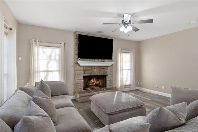 living room featuring ceiling fan, a stone fireplace, wood finished floors, and baseboards