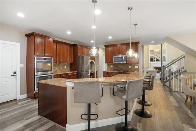 kitchen featuring light stone counters, appliances with stainless steel finishes, a breakfast bar, and light wood-style flooring