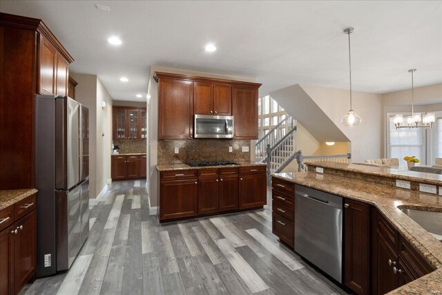 kitchen featuring light stone counters, light wood-style floors, appliances with stainless steel finishes, tasteful backsplash, and decorative light fixtures