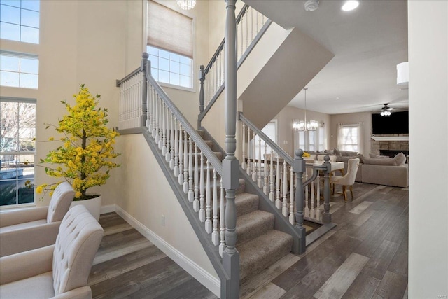 stairway featuring ceiling fan with notable chandelier, a fireplace, baseboards, and wood finished floors