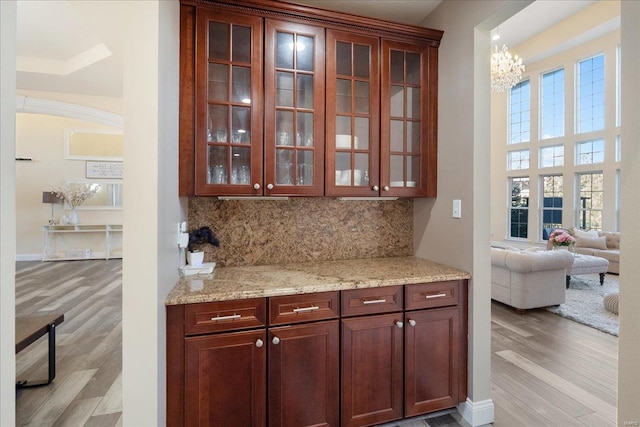 bar with light wood-style floors, baseboards, decorative backsplash, and an inviting chandelier