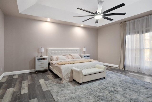 bedroom with recessed lighting, dark wood-type flooring, a ceiling fan, baseboards, and a tray ceiling