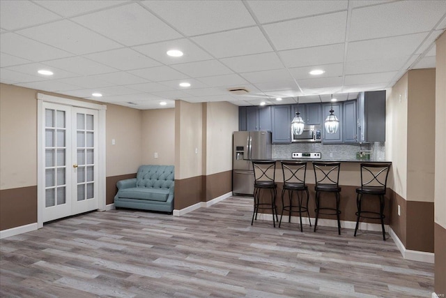 bar with french doors, pendant lighting, stainless steel appliances, tasteful backsplash, and light wood-style floors